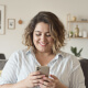 Woman smiling while looking at her smartphone indoors.